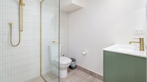 Een moderne badkamer met een douche in een glazen cabine, een wit toilet en een wastafel met een groen kastje.