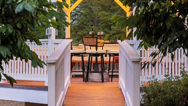 A wooden deck leading to a covered outdoor seating area with a white picket fence and a decorative light fixture. - Movie Theater • Tennis • Barrel Sauna • Hot Tub (Templeton)