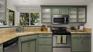 A kitchen with green cabinets, stainless steel appliances, a granite countertop, and a window with a view of trees. - Movie Theater • Tennis • Barrel Sauna • Hot Tub (Templeton)