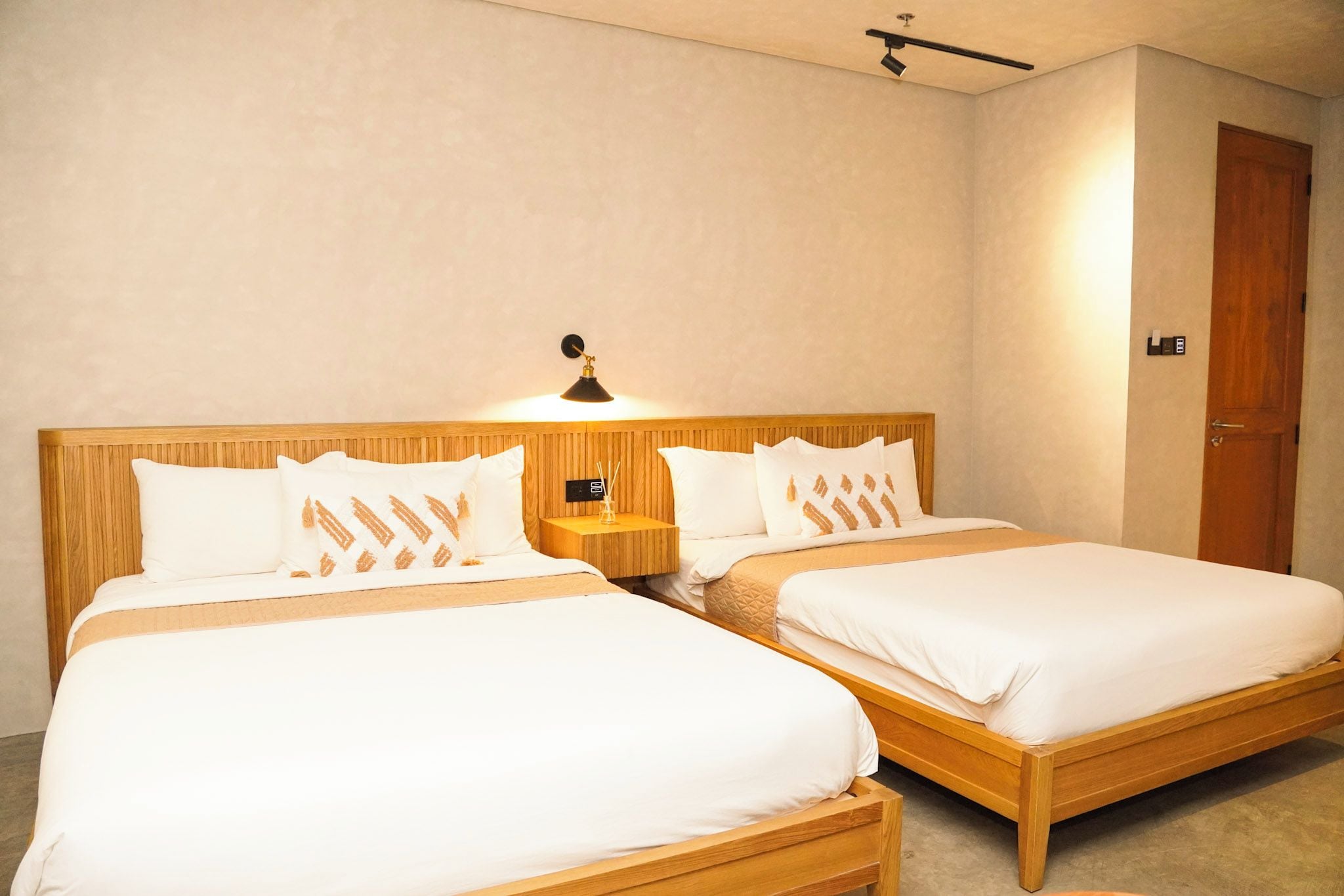 Een hotelkamer met twee enkele bedden, een houten hoofdbord, een nachtkastje met een lamp en een deur.