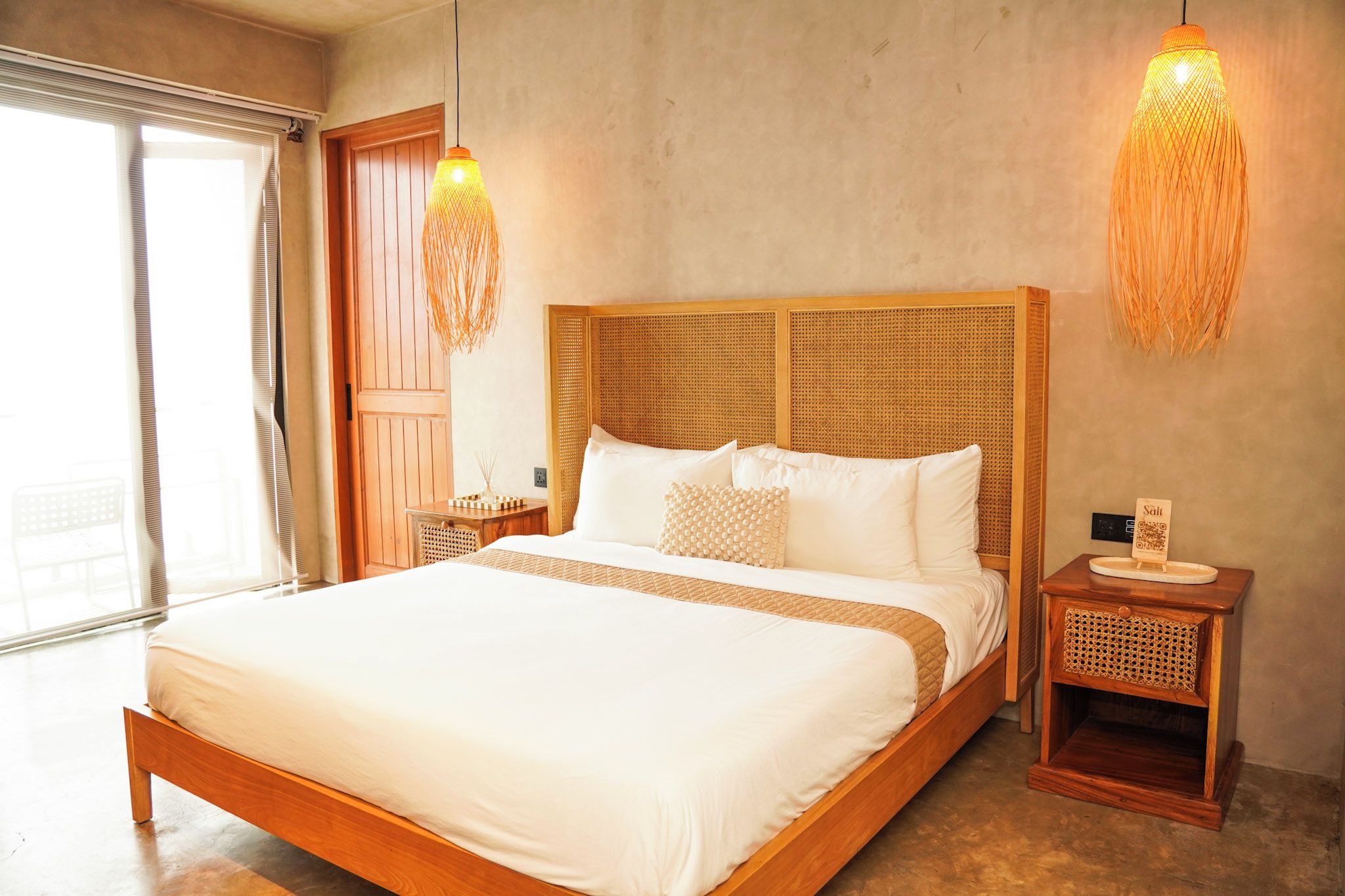 Une chambre à coucher avec un grand lit, une tête de lit en bois, des tables de chevet et une fenêtre avec des stores.