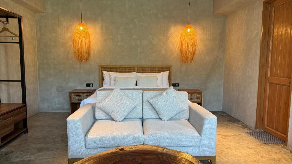 A bedroom with a bed, two bedside tables, a sofa, and a hanging light fixture.
