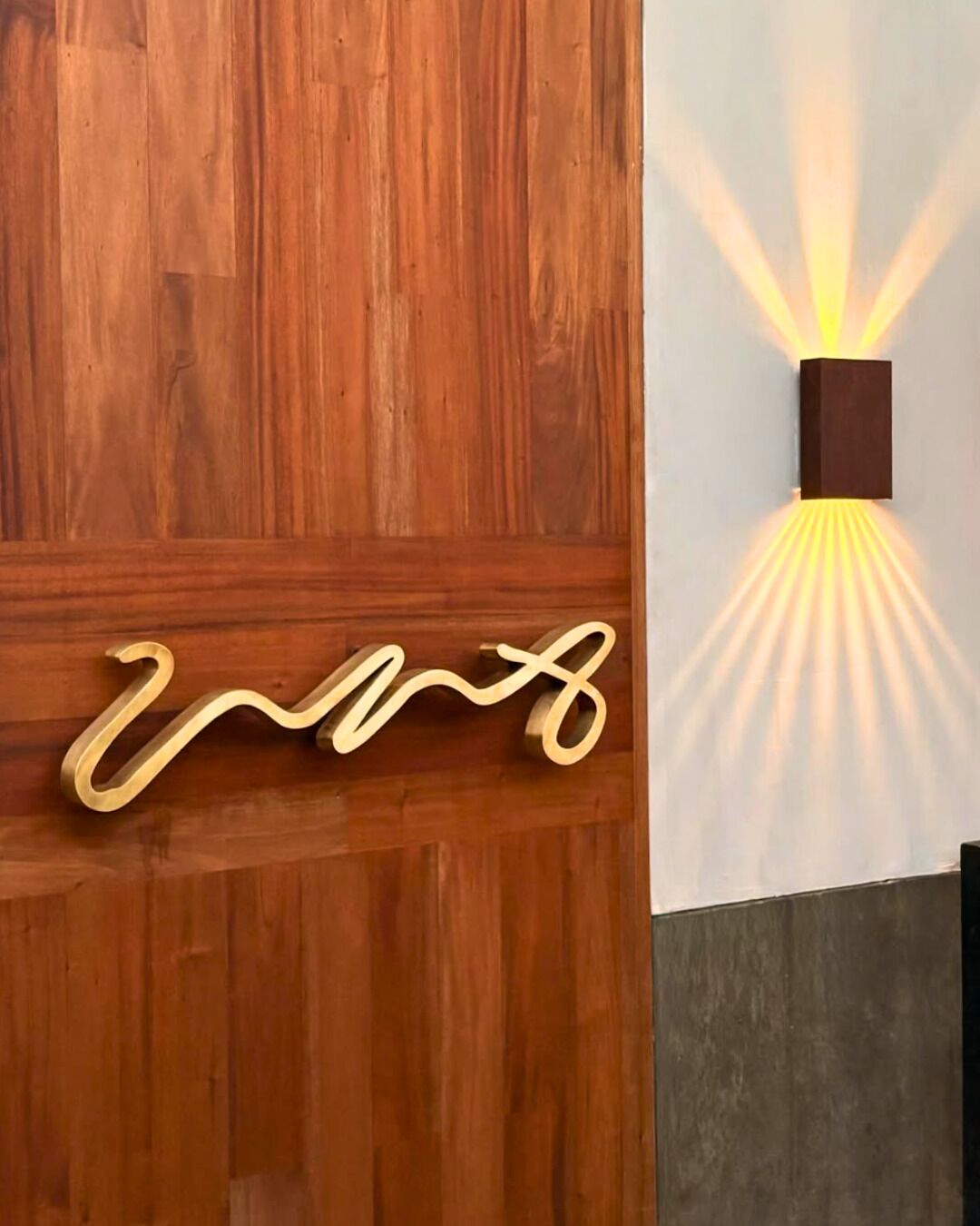 Pared de madera con una lámpara moderna y un letrero metálico decorativo.