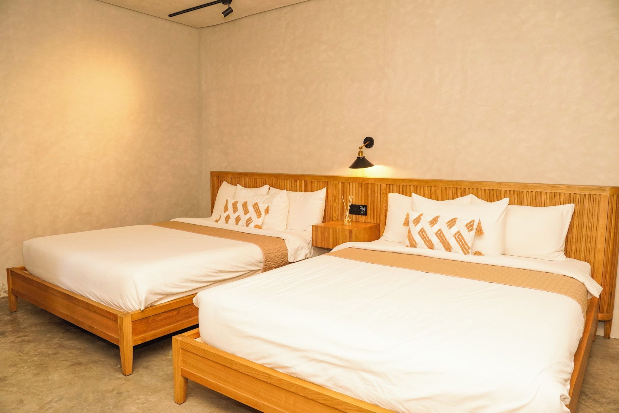 Quarto de hotel com duas camas de madeira, cada uma com roupa de cama branca e almofadas estampadas.