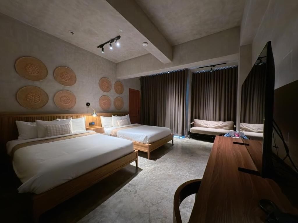A hotel room with two beds, a desk, a TV, and a wall with circular patterns.