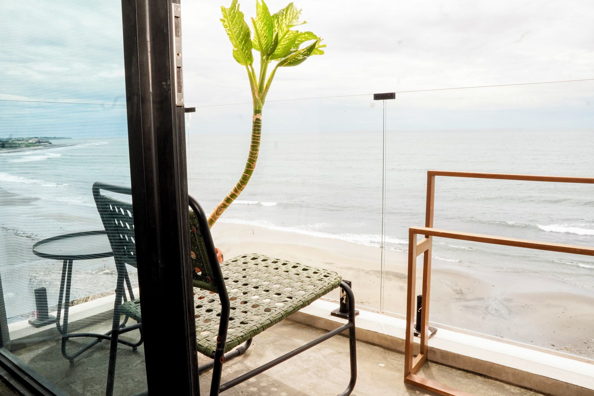 A balcony with a view of the beach and ocean, a chair, and a table.