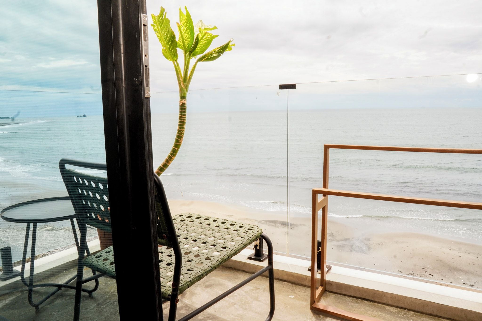 Un balcón con vista al mar, una silla, una mesita y una planta en maceta.