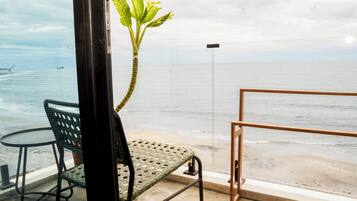 Un balcón con vista al mar, una silla, una mesita y una planta en maceta.