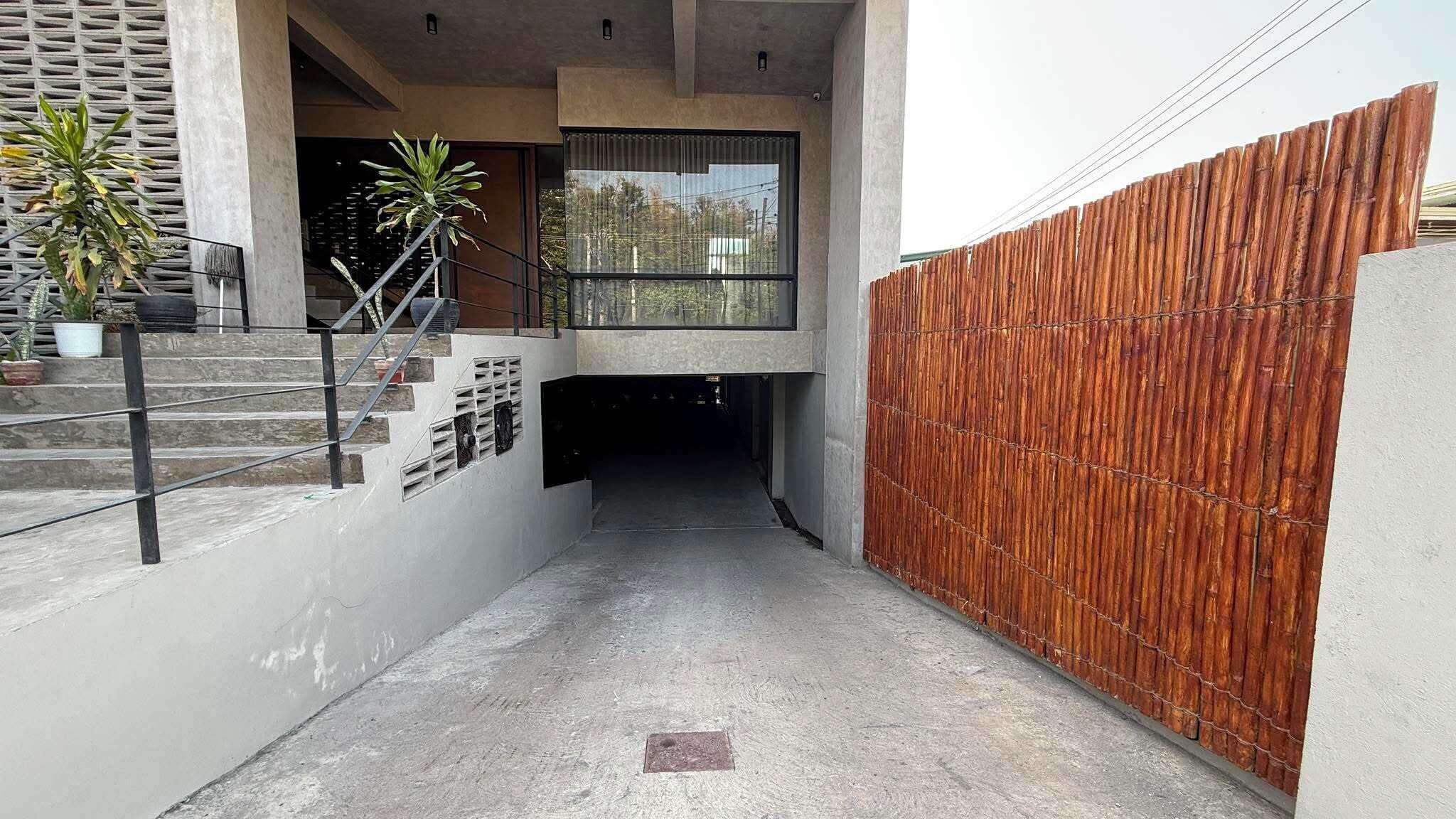 A narrow concrete pathway leading to a building entrance with a wooden fence on one side and a staircase on the other.