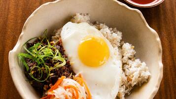 A bowl of rice topped with a fried egg, shredded carrots, and a dark condiment, possibly a sauce or relish.
