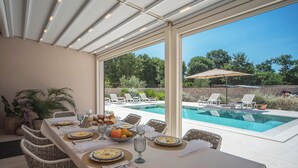 Ein Essbereich im Freien mit Blick auf einen Pool, Tischdecken sind weiß.