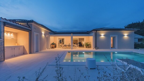 Ein modernes Haus mit Schwimmbad, Sitzgelegenheiten im Freien und einem gut beleuchteten Patio.
