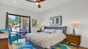 Um quarto com cama, duas mesas de cabeceira, um ventilador de teto, uma janela grande e vista para o exterior.