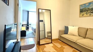A living room with a sofa, a television, a mirror, and a dining area with chairs and a table.