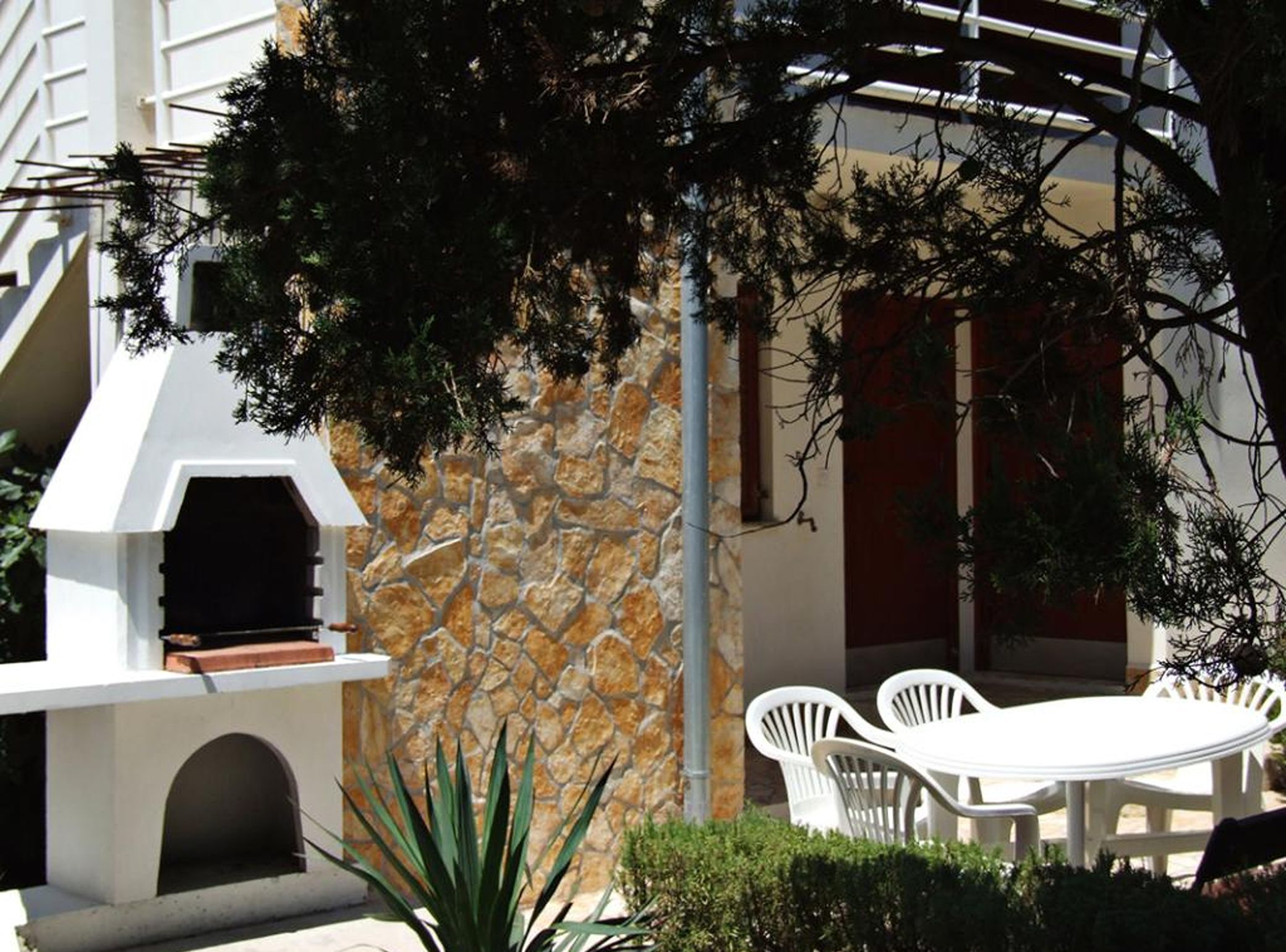 An outdoor seating area with a stone wall and a white grill structure.