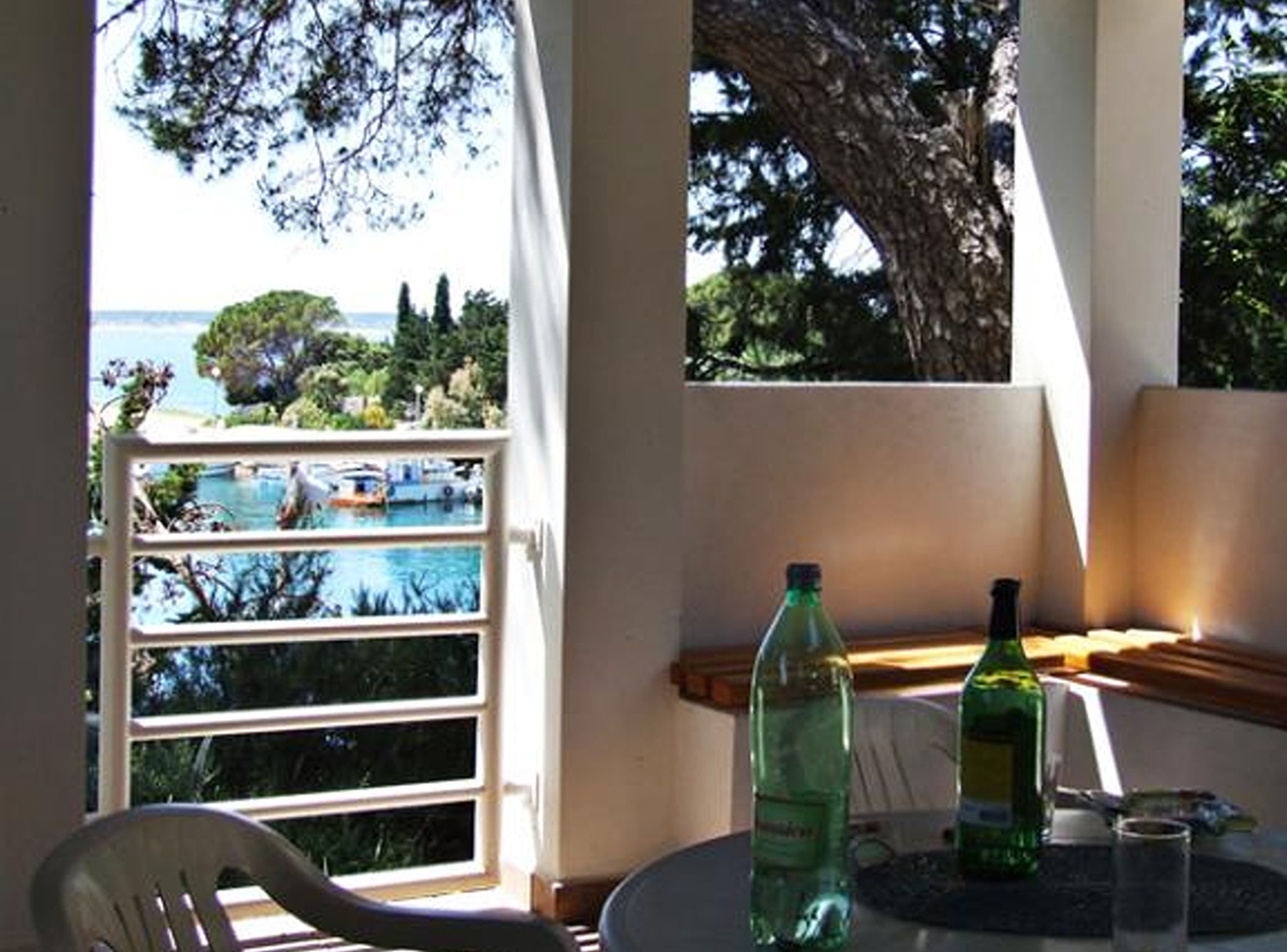 A balcony with a view of the sea, a chair, and two bottles on a table.