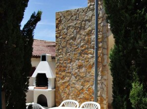 Eine Steinsäule, ein weißer Außenofen und weiße Stühle.