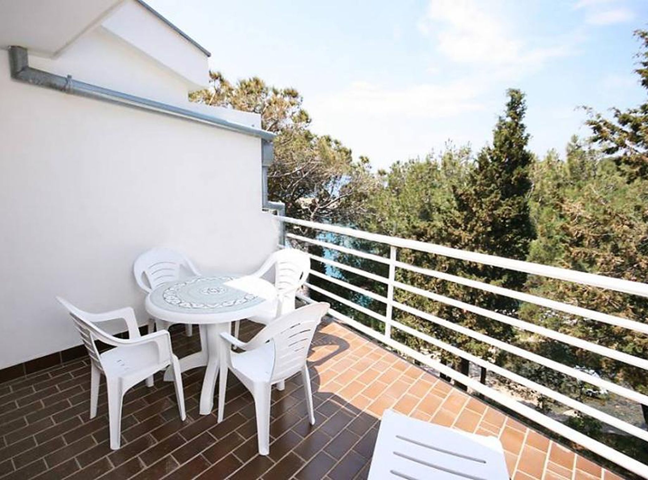 Een balkon met een witte tafel en stoelen, een witte balustrade en uitzicht op bomen en de lucht.
