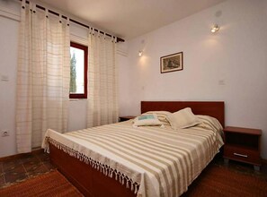 Un dormitori amb llit, una tauleta de nit, una finestra amb cortines i un quadre penjat a la paret.