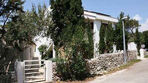 A white building with a stone wall and a gate, surrounded by trees and a clear sky. - Apartments by Seni (Kolan)
