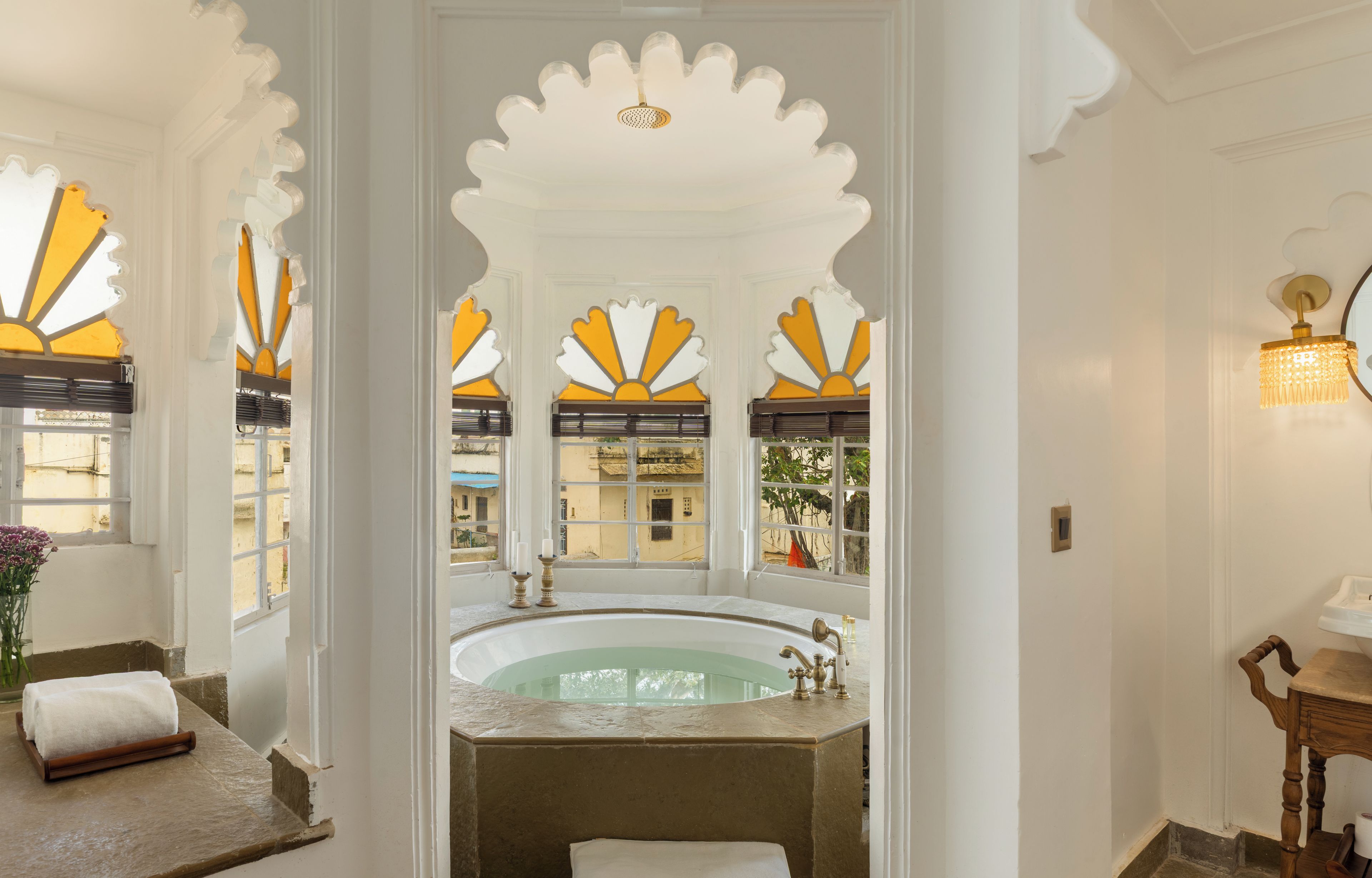 Une salle de bain avec une baignoire, un lavabo et un miroir. Les murs sont décorés et il y a une fenêtre donnant sur les bâtiments à l’extérieur.