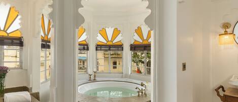 Une salle de bain avec une baignoire, un lavabo et un miroir. Les murs sont décorés et il y a une fenêtre donnant sur les bâtiments à l’extérieur.