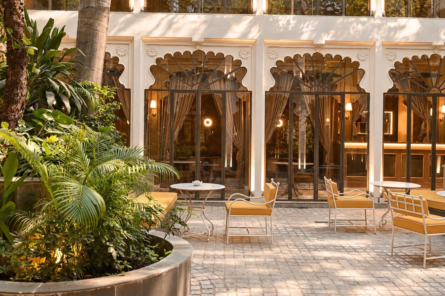 An outdoor seating area with tables and chairs, surrounded by lush greenery and architectural details.