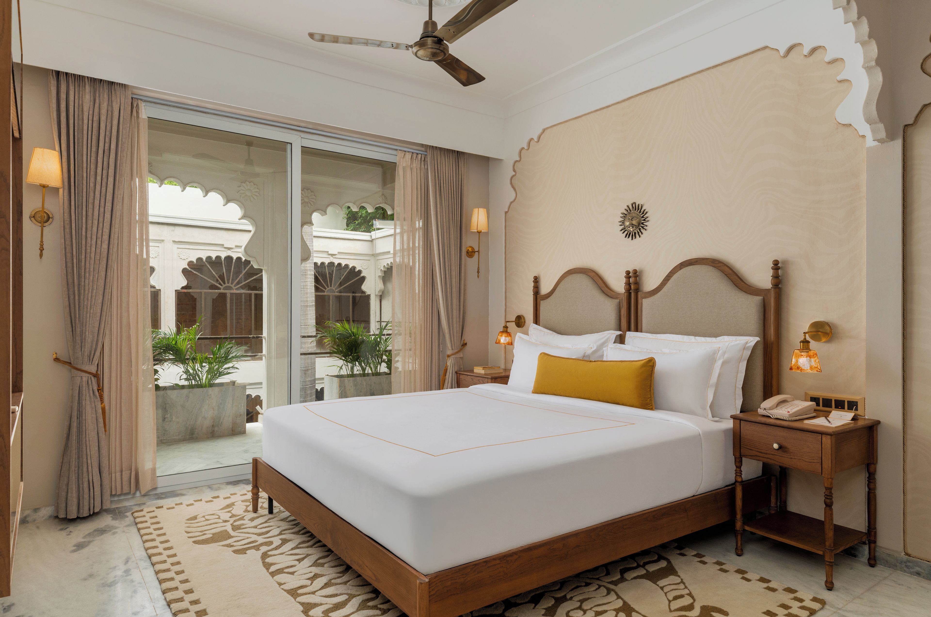 A hotel room with a large bed, a wooden headboard, a nightstand, a telephone, and a wall-mounted lamp.