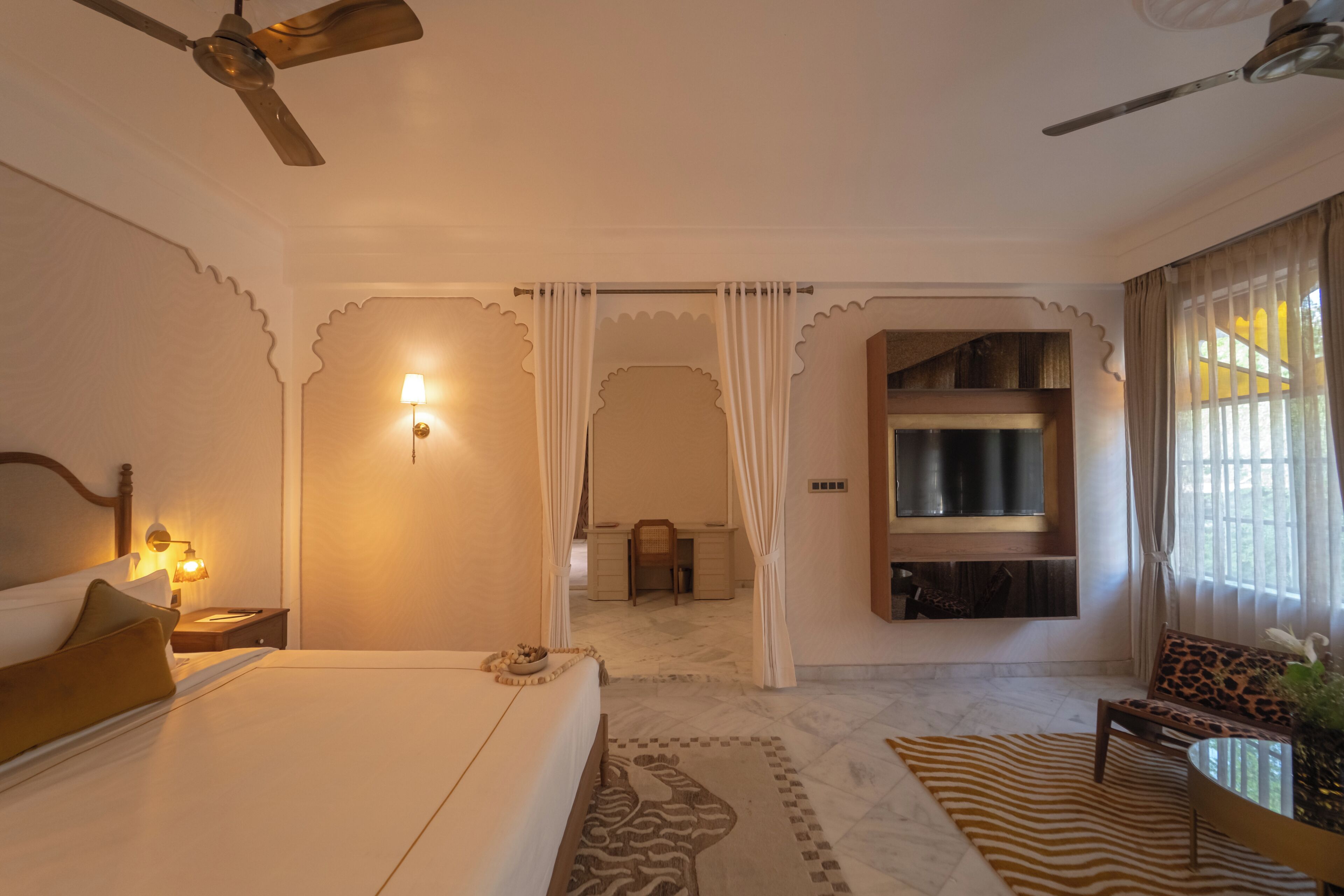 Une chambre d’hôtel équipée d’un lit, d’un bureau, d’une chaise, d’un ventilateur de plafond et d’un téléviseur fixé au mur.