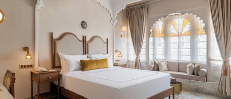 A hotel room with a large bed, a bedside table with a lamp, a window with curtains, and a view of the outside.
