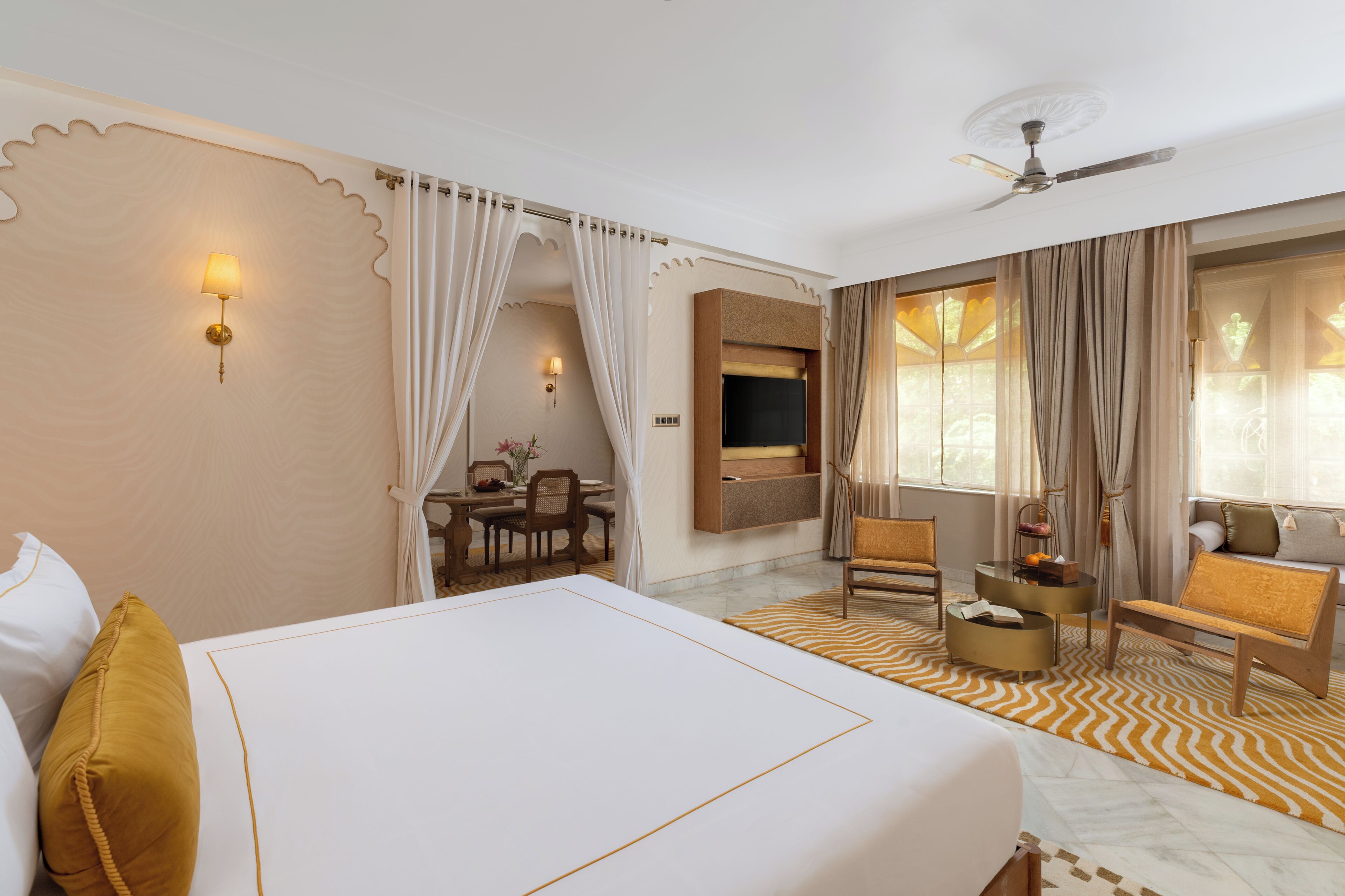 Habitación de hotel con una cama grande, un escritorio con silla, un televisor montado en la pared y un ventilador de techo.