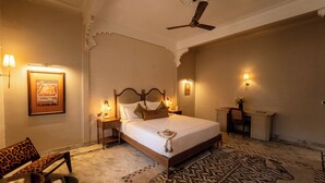 A hotel room with a bed, a desk, a chair, a ceiling fan, and a patterned rug.