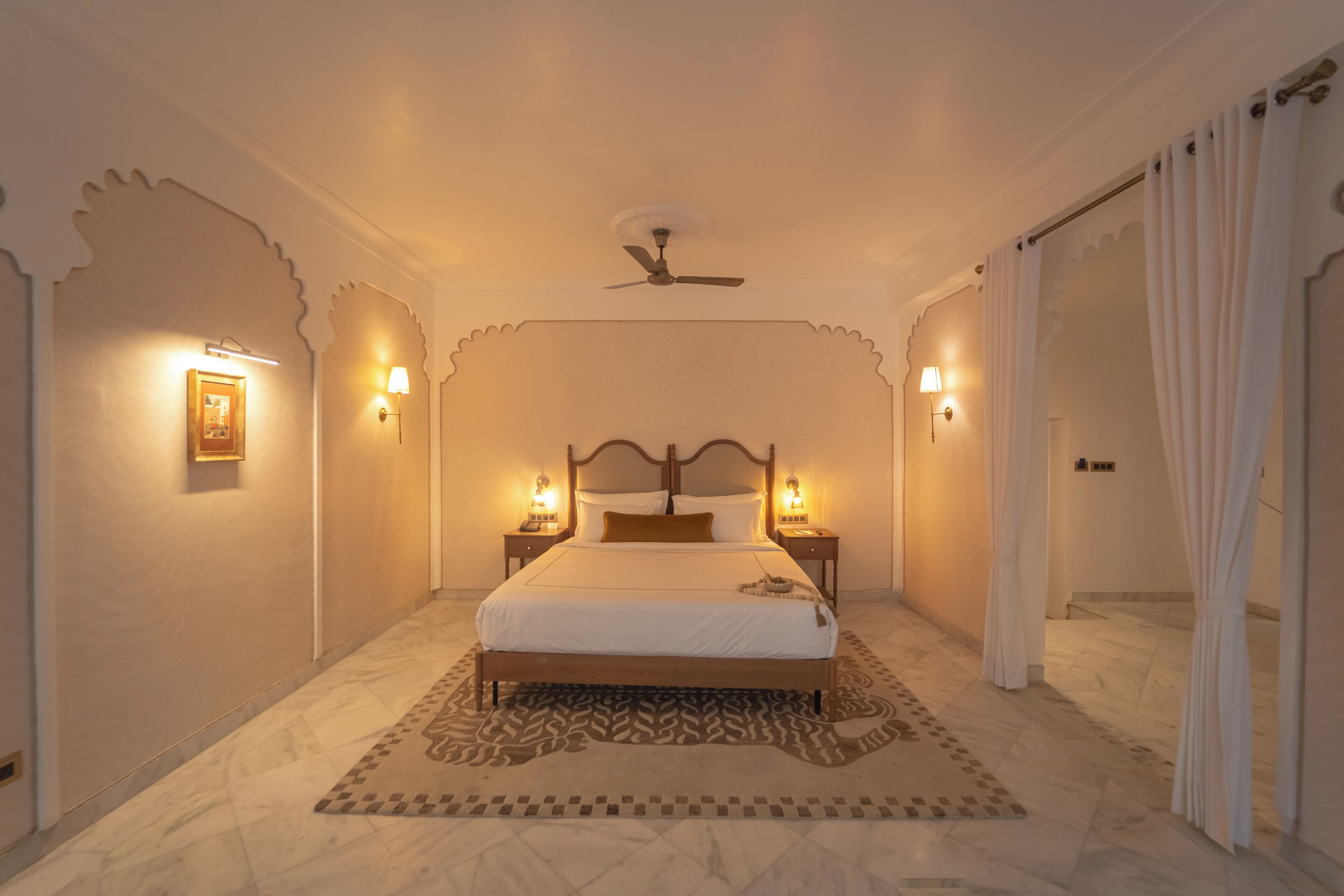 A bedroom with a bed, two bedside tables, a ceiling fan, and a patterned rug.