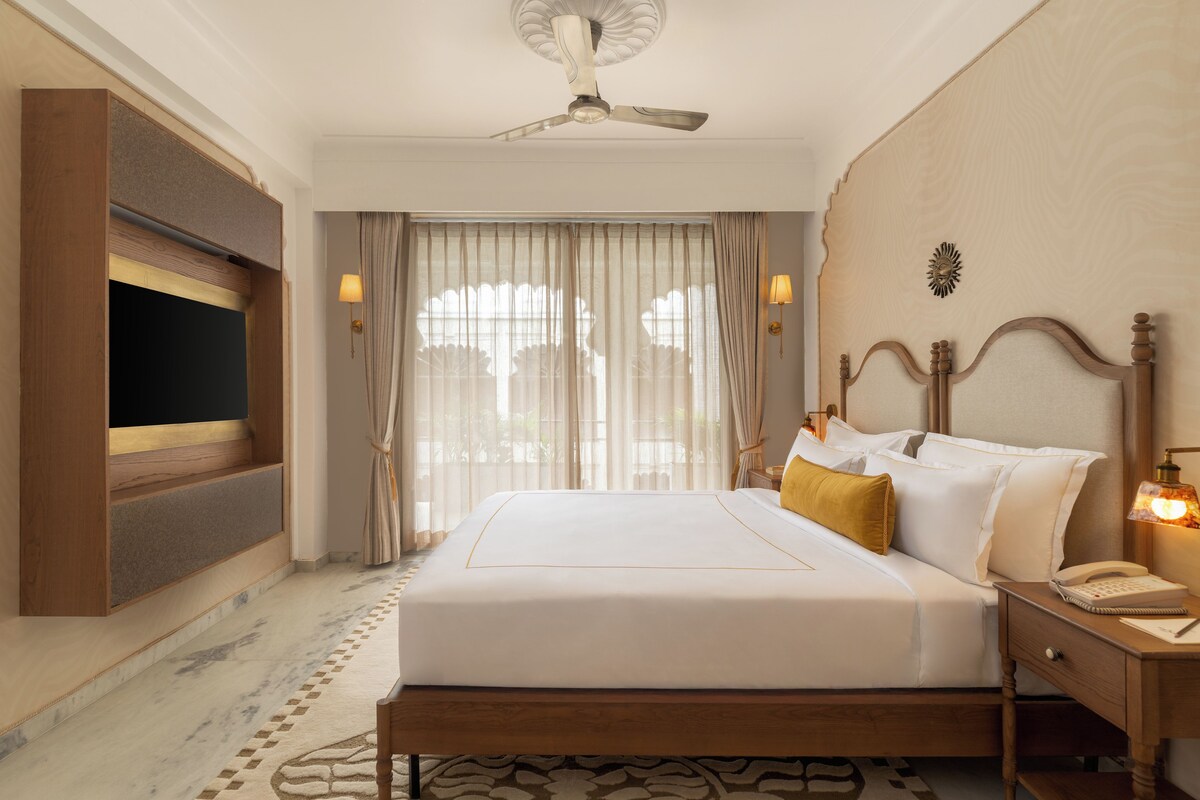 Quarto de hotel com cama, mesa de cabeceira com abajur, televisão na parede e ventoinha no teto.