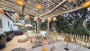 An outdoor deck with wooden furniture, a table with drinks, and a pergola with hanging lights. - Les Yeux Bleus: Bohemian Cottage, Petanque, and Spa, 25 Minutes from the Sea (Restinclières)