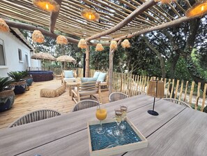 Eine Terrasse im Freien mit Holzmöbeln, einem Tisch mit Getränken und einer Pergola mit hängenden Lichtern.