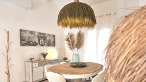 A dining area with a round wooden table, white chairs, a hanging light fixture, and a decorative wall piece. - Les Yeux Bleus: Bohemian Cottage, Petanque, and Spa, 25 Minutes from the Sea (Restinclières)