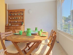 A dining area with a round wooden table, green and yellow ceramic dishes, and matching chairs. - Le Grand Parc by Interhome (Saint Aygulf)