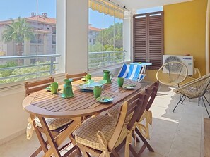 A balcony with a wooden table, chairs, and a fan. - Le Grand Parc by Interhome (Saint Aygulf)