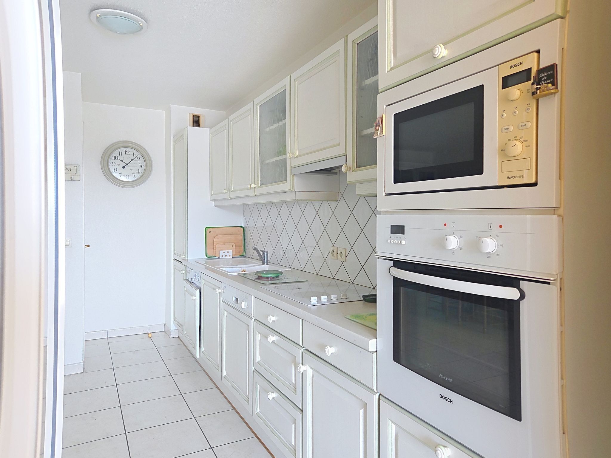 A kitchen with white cabinets, a microwave, an oven, a clock, and a tiled backsplash.