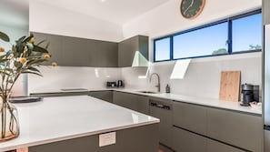 A modern kitchen with grey cabinets, a white countertop, a built-in dishwasher, a coffee machine, and a window with a view.
