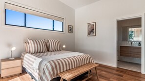 A bedroom with a bed, bedside tables, a bench, a window, and a bathroom visible through an open door.