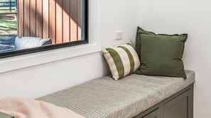 Assento junto à janela com almofadas listradas e vista para um deck de madeira.