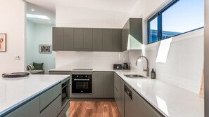 Eine kompakte Küche mit grauen Schränken, einem eingebauten Backofen, einem Geschirrspüler und einem Fenster, das für natürliches Licht sorgt.