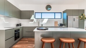 A modern kitchen with grey cabinets, a central island with stools, a window above the sink, and a clock on the wall.