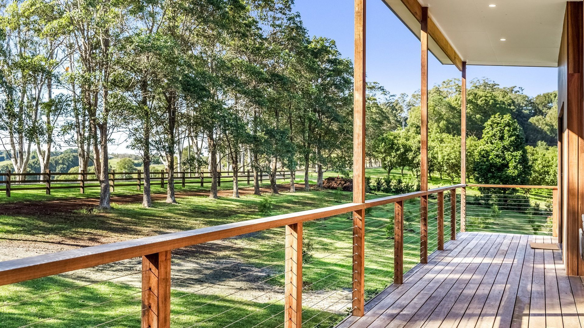 Una terraza de madera con barandilla metálica que da a un espacio verde con árboles.