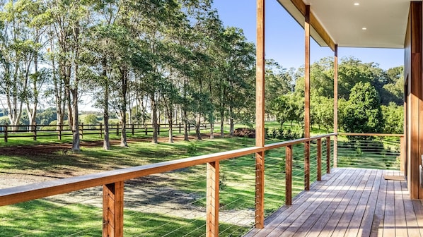 A wooden deck with a metal railing overlooking a grassy area with trees.