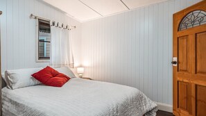 Een slaapkamer met een bed, een raam met gordijnen, een bedlampje en een houten deur.