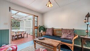 Een gezellige kamer met een houten bankje, een tafel en zicht door een glazen deur op een buitenruimte met een tafel en stoelen.