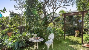 A garden with a round metal table, a white chair, and a pergola.